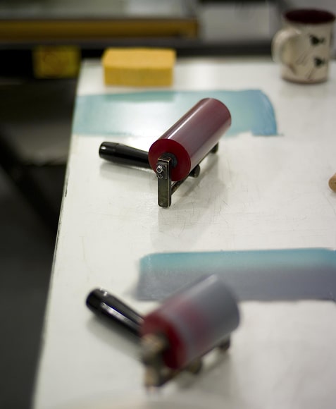 red rubber brayer roller on white table with inked squeegee strips front view flat lay in print studio